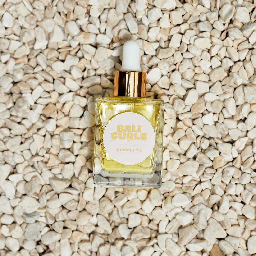 Small bottle OF BALI CURLS BONDING OIL with dropper on a textured beige surface
