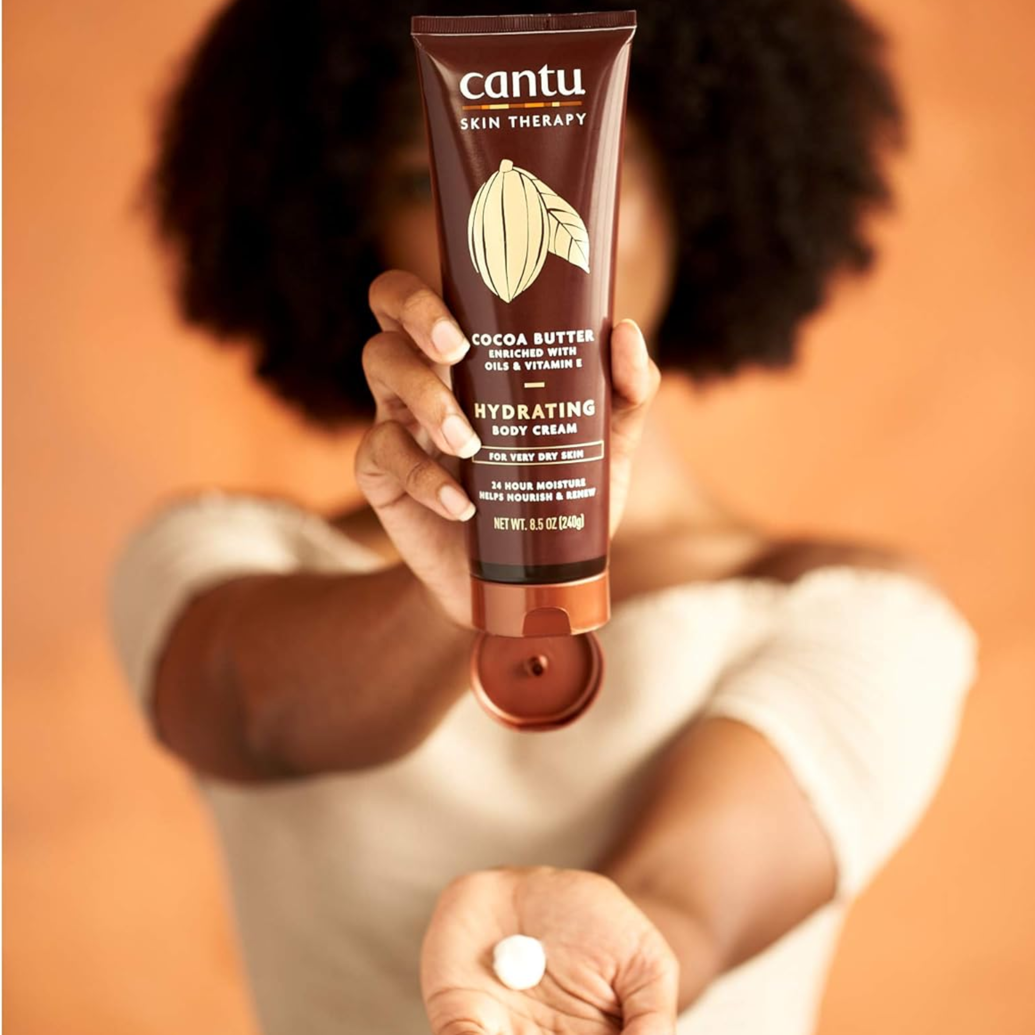 Cantu Skin Therapy Shea Butter Hydrating Body Cream 240g model holding body cream tube squeezing into her hand