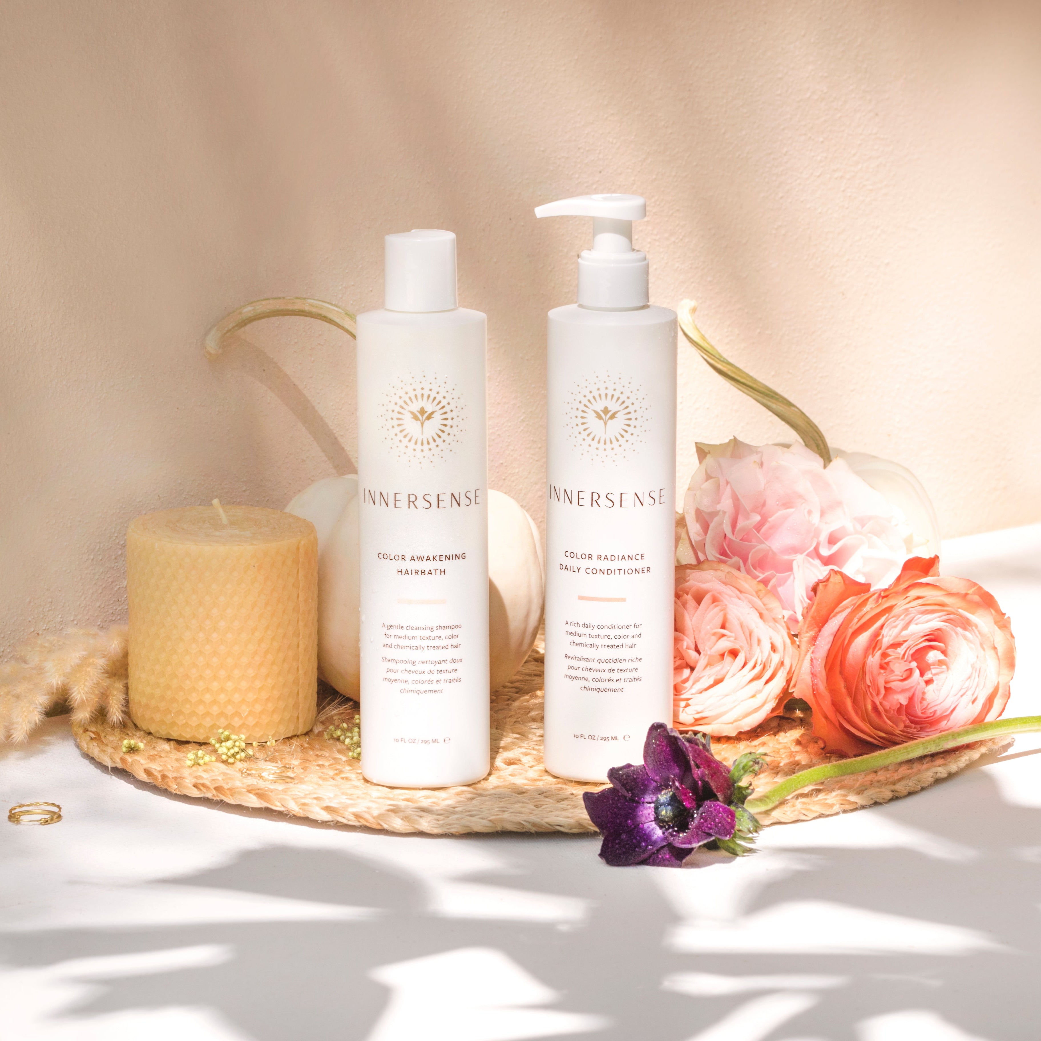 Two bottles of Innersense skincare products on a woven mat with flowers and a candle.