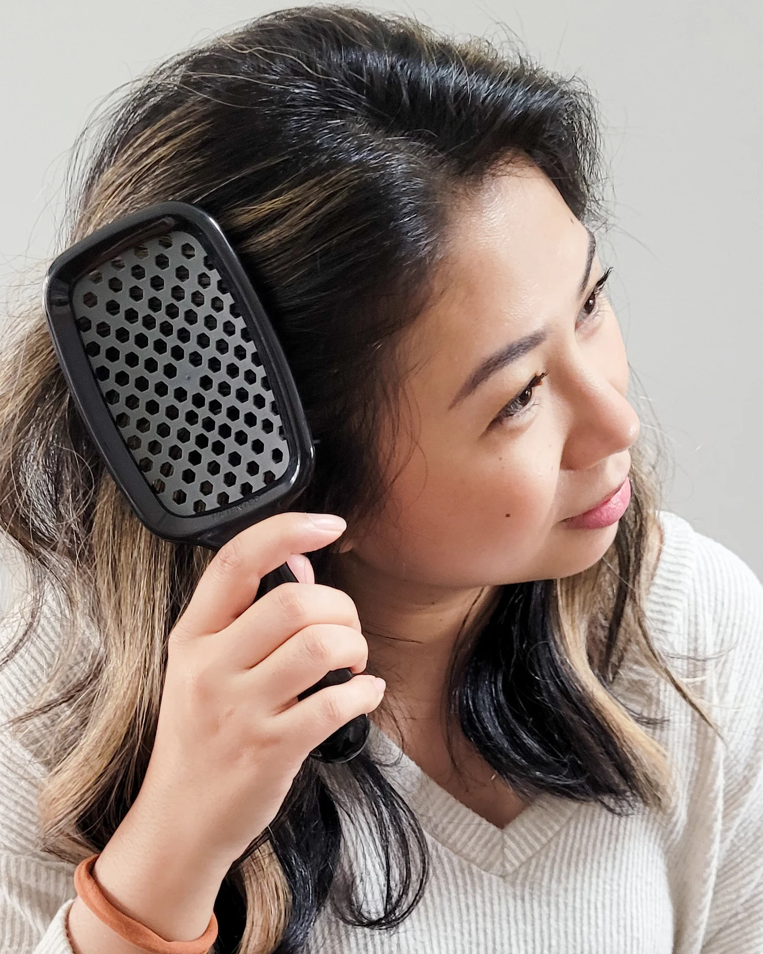 Woman using unbrush hair detangler brush on her hair against a neutral background