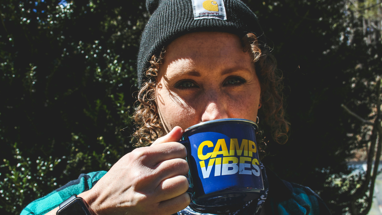 curly woman wearing beanie and drinking from mug