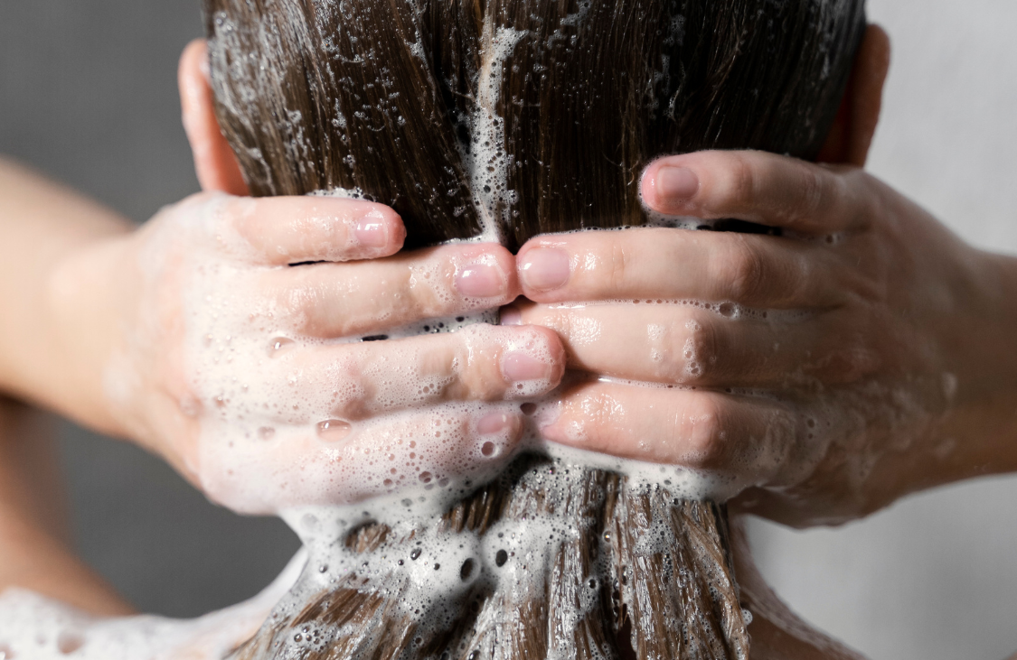 how often to wash your hair? woman washing her hair with shampoo in a shower