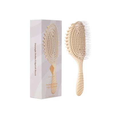A light natural wood paddle hairbrush shown next to its white and pale pink packaging box on a plain white background by Bounce Curl. 