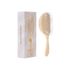 A light natural wood paddle hairbrush shown next to its white and pale pink packaging box on a plain white background by Bounce Curl. 