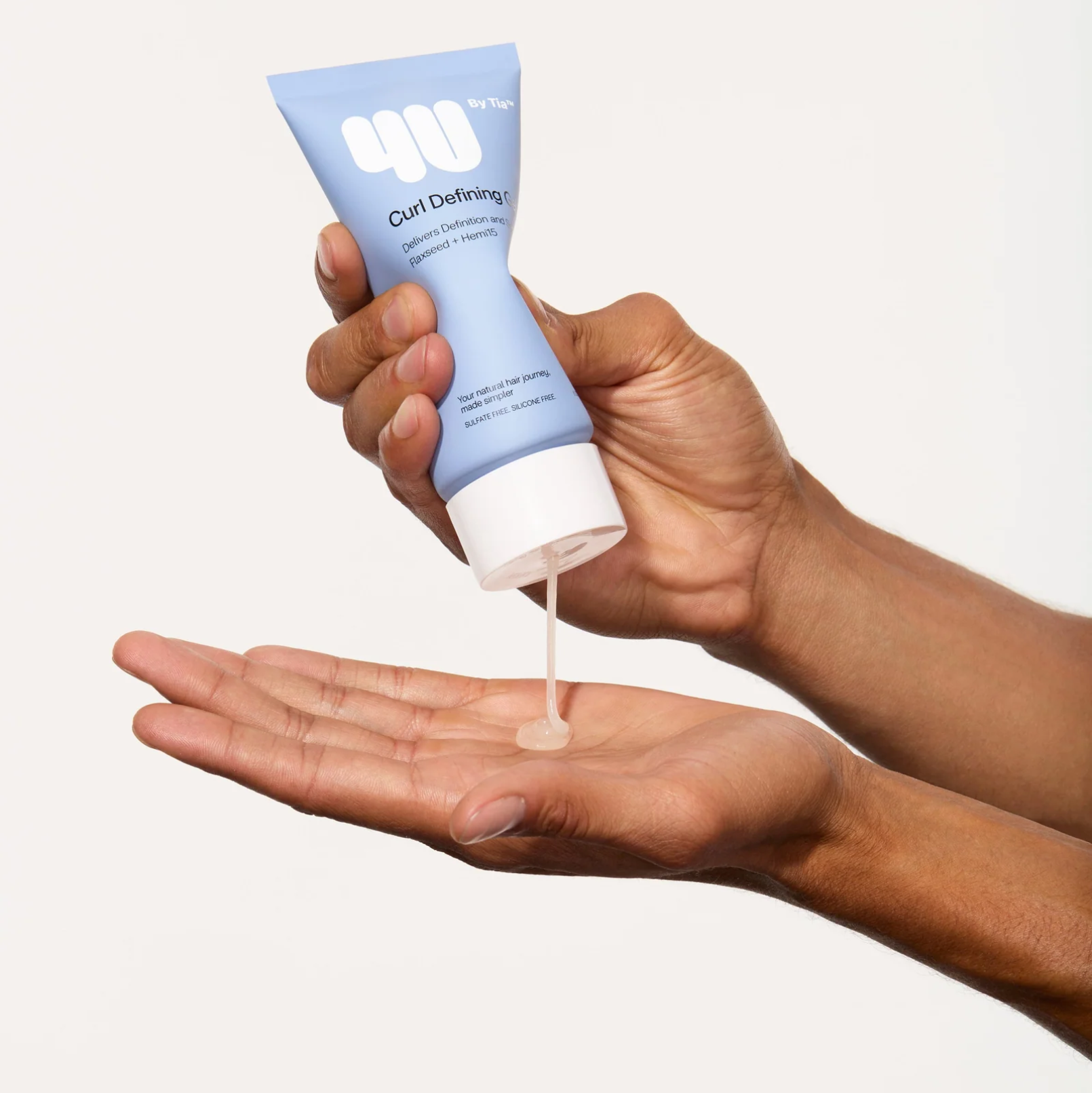 Hand holding a tube of 'Curl Definer' with product being dispensed onto the palm against a white background