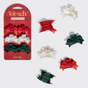 A 3-piece hair claw clip set by Kitsch, featuring red, white, and green satin ribbon bows, shown both in its retail blister packaging and individually on a light gray background.