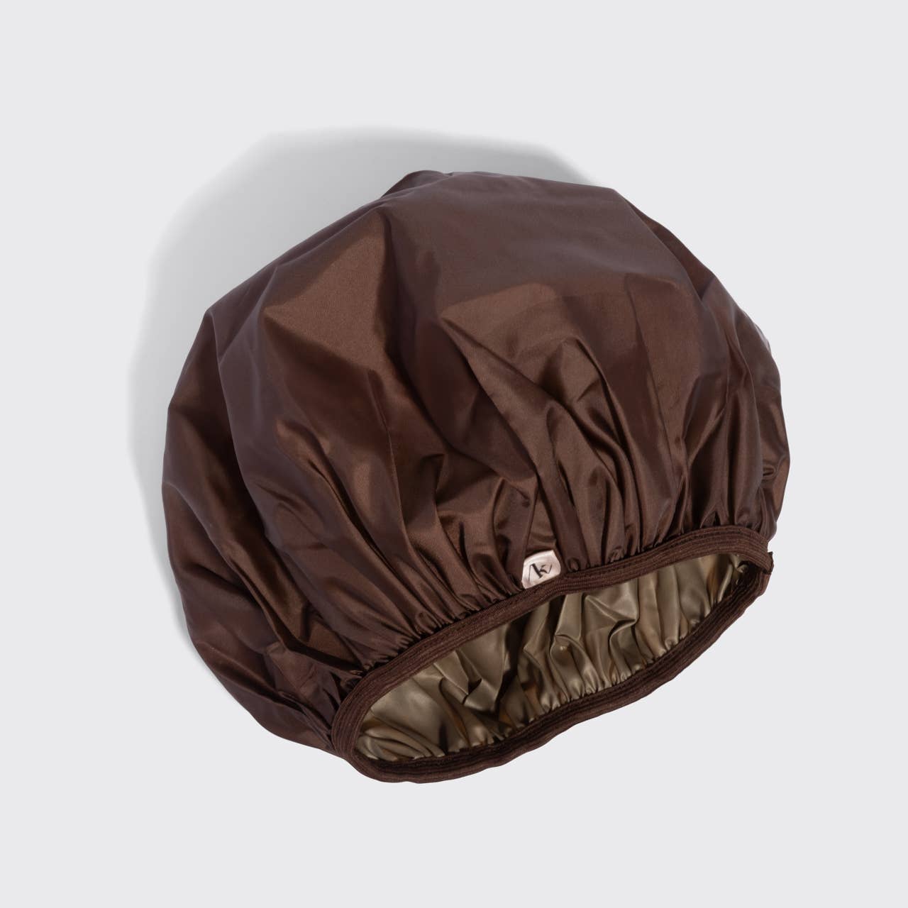 A dark brown nylon shower cap with an elasticized opening and a small white brand tag, shown on a light gray background.