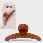 A translucent amber-brown arched hair claw clip shown in front of its light pink Kitsch retail card packaging on a light gray background.