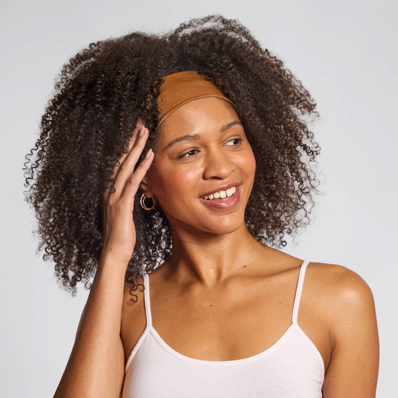 Woman wearing a white tank top with a plain background and Kitsch active headband in colour sedona