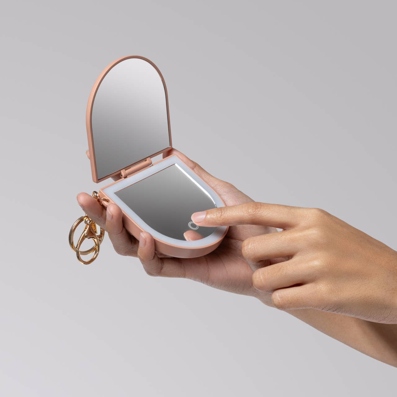 Hand holding a compact mirror with a light on a gray background