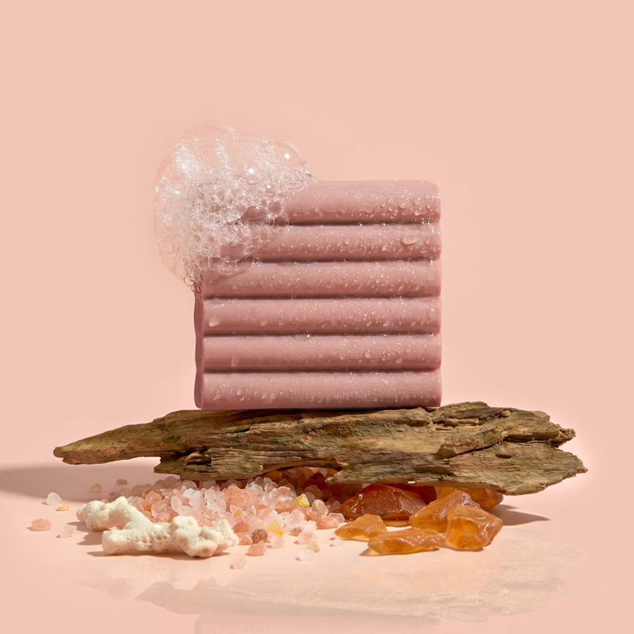 Stack of Kitsch Amber Shores Body Wash Bar  on a wooden platform with decorative elements on a pink background