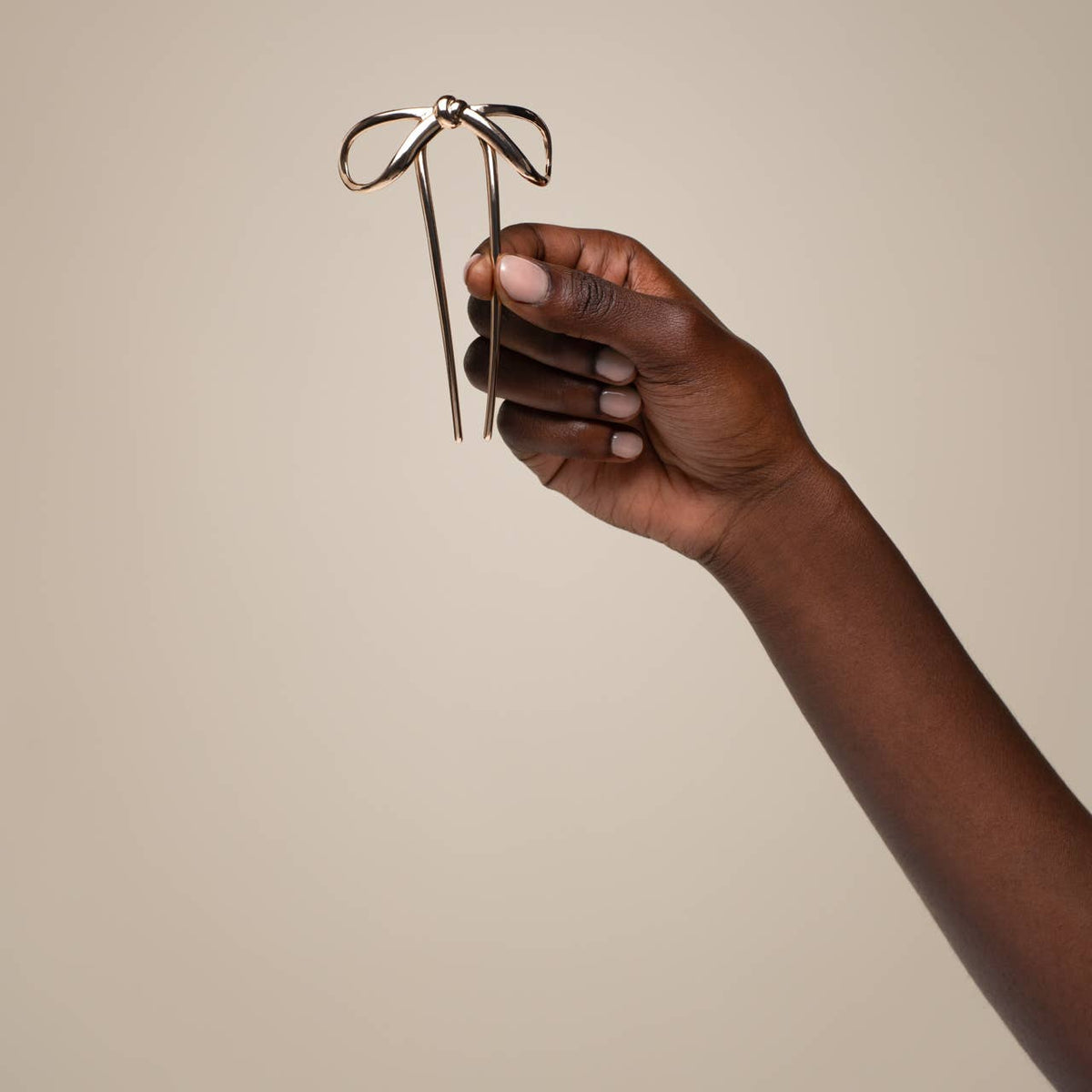 Hand holding a Kitsch Mini Metal Bow French Hair Pin – Gold against a beige background