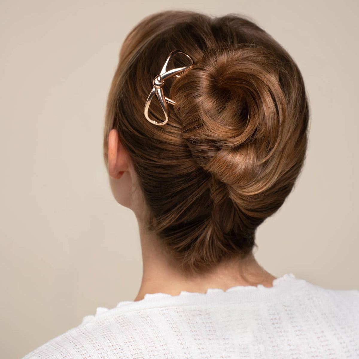 Woman with styled hair bun wearing a white sweater against a beige  background