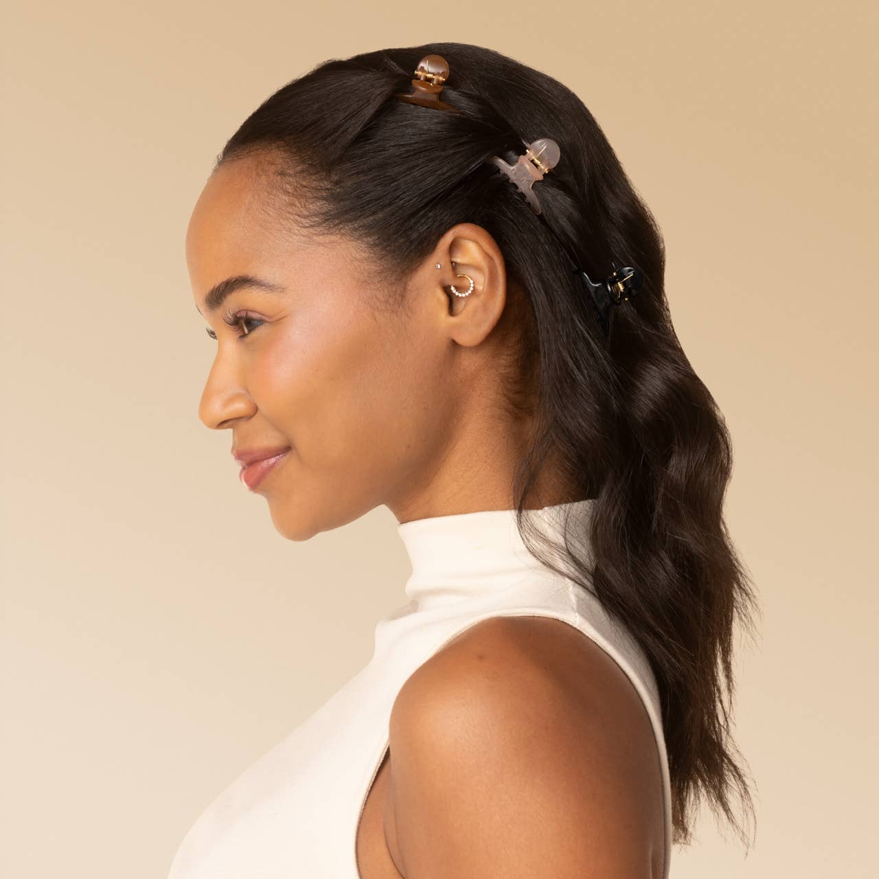 A woman in profile wearing three small hair clips in her dark hair, against a solid beige background.