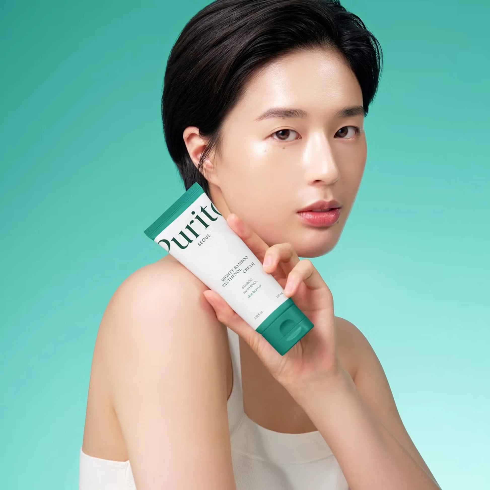 Woman holding a Purito skincare product against a teal background