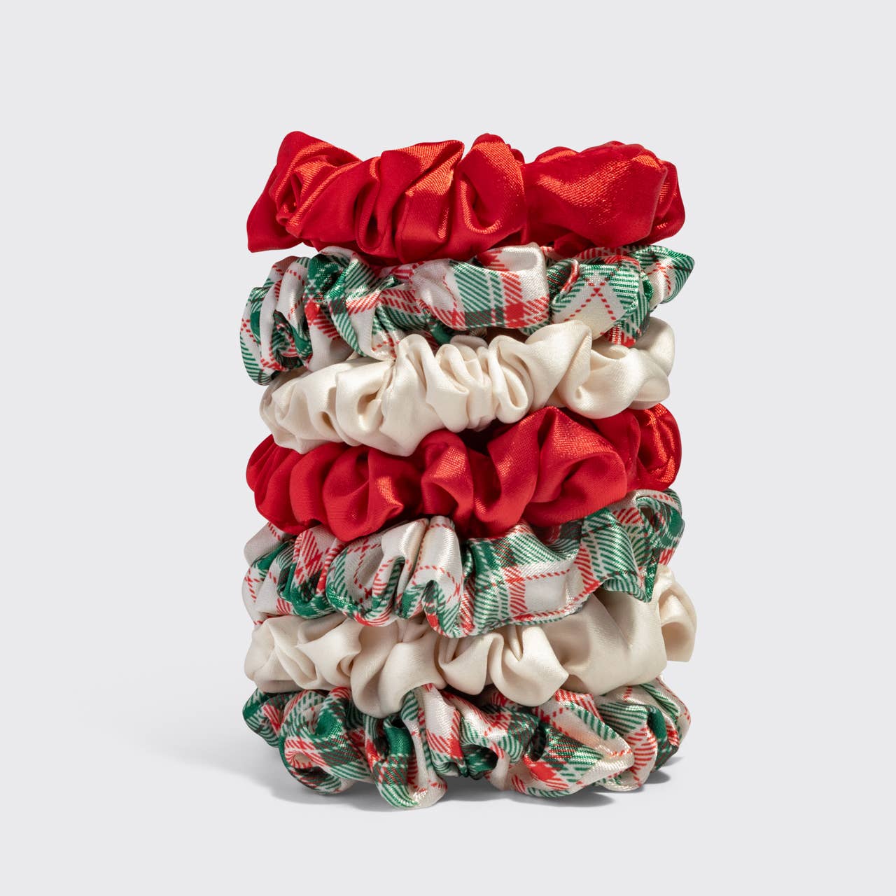 A stack of ten fabric hair scrunchies in red, cream, and green plaid, arranged vertically on a light gray background.