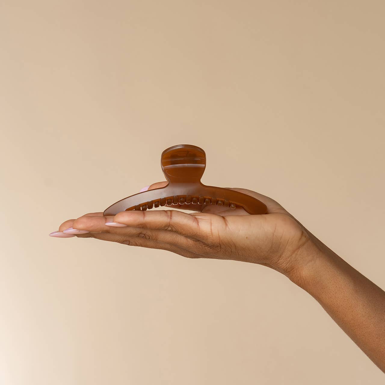 A translucent amber-brown hair claw clip held in the palm of a hand against a solid beige background.