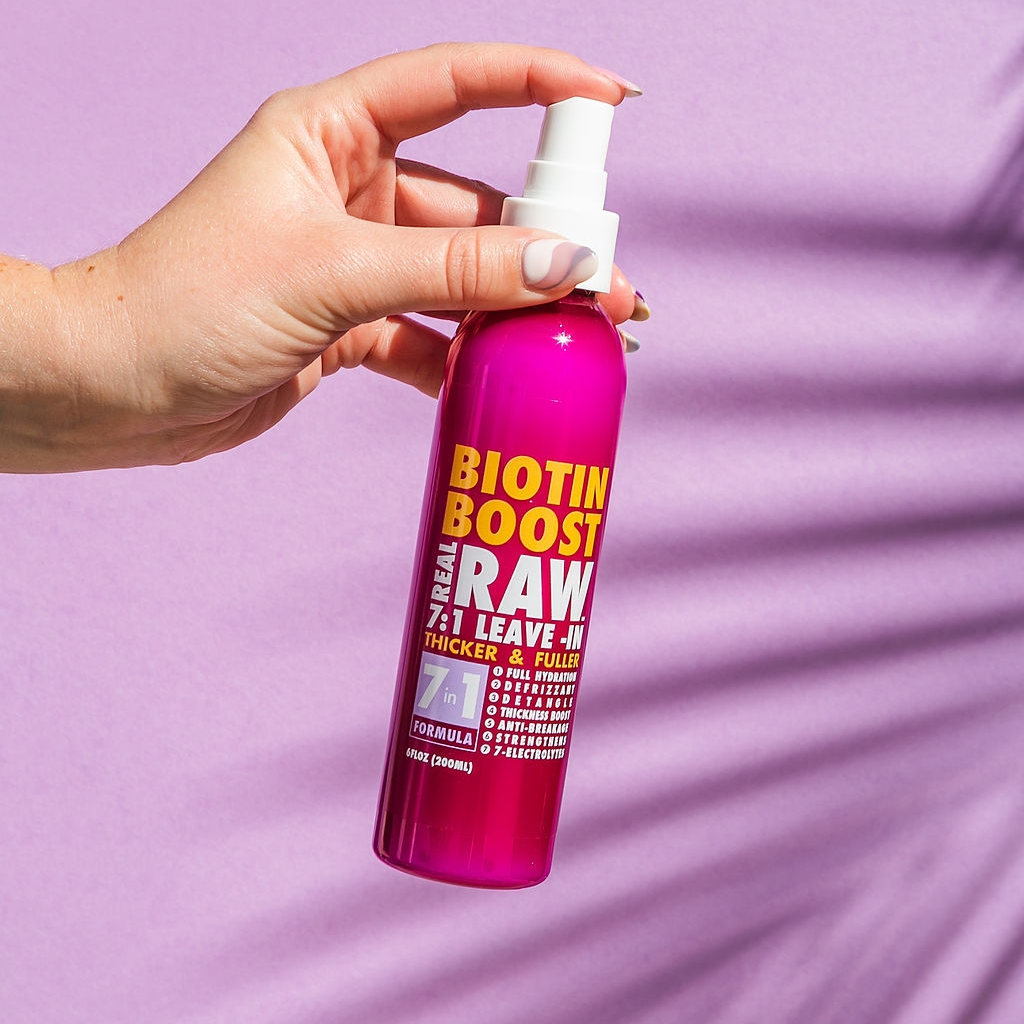Hand holding a pink bottle labeled 'Biotin Boost Raw' against a purple background