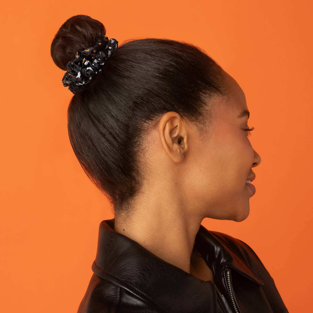 A woman in profile wearing a black embellished scrunchie, shown against a solid orange background. Kitsch Ghost & Pumpkins Scrunchies