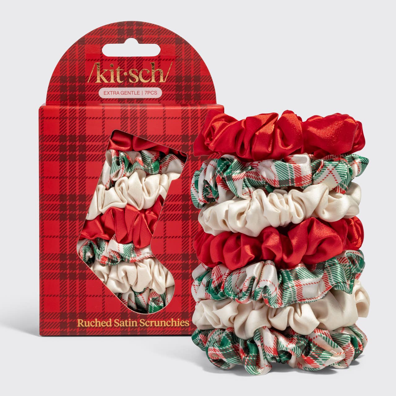 A set of five Kitsch ruched satin scrunchies displayed next to their red plaid retail packaging. The scrunchies feature a mix of solid red satin, cream satin, and green and red plaid ribbons.