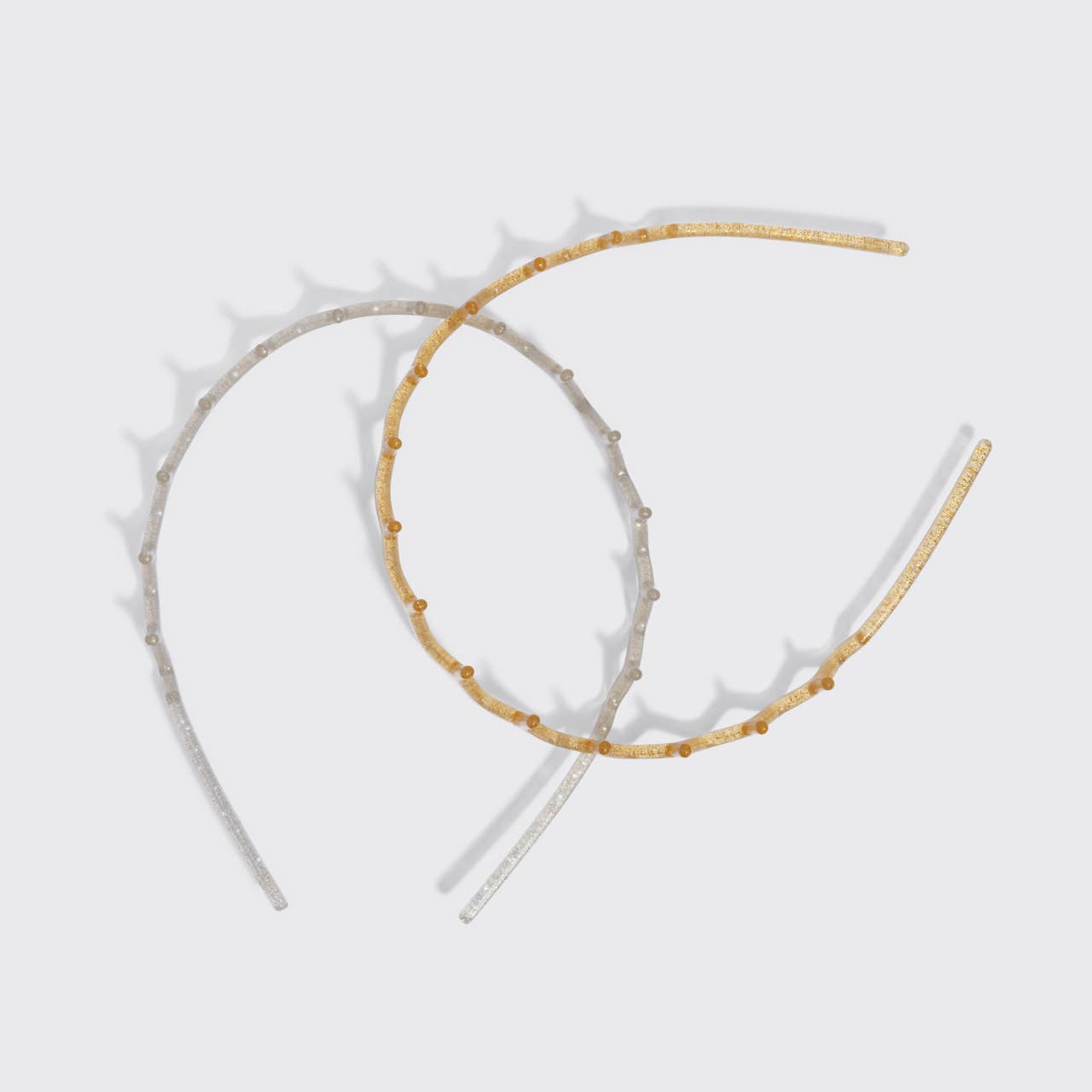 Two thin decorative headbands with small evenly spaced studs, one in champagne gold and one in champagne silver, displayed on a light gray background.