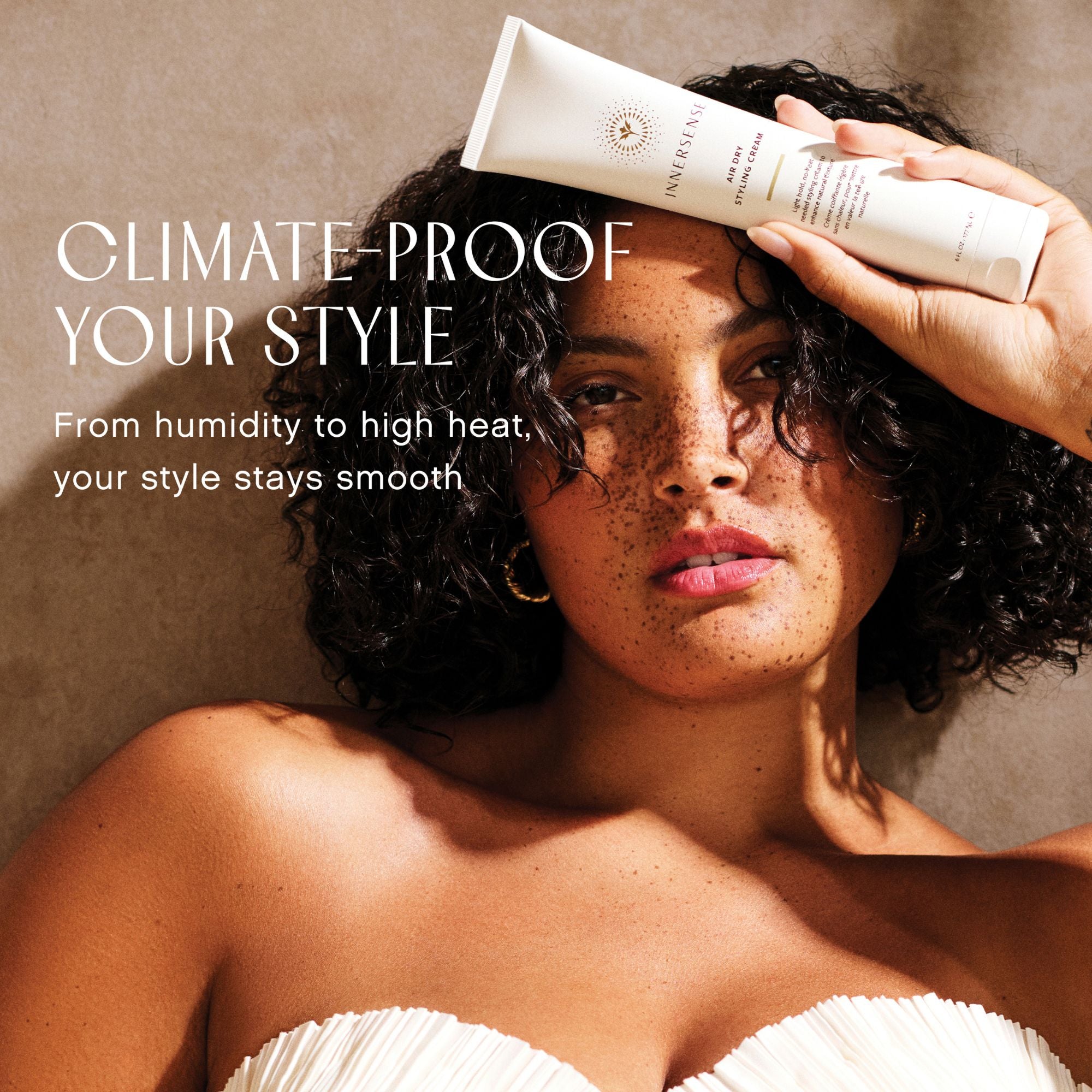 Woman holding a Innersense Air Dry Styling Cream hair product with text about climate-proof hair style.