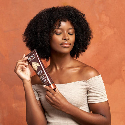 Cantu Skin Therapy Shea Butter Hydrating Body Cream 240g model holding body cream tube looking down on a red sand coloured background