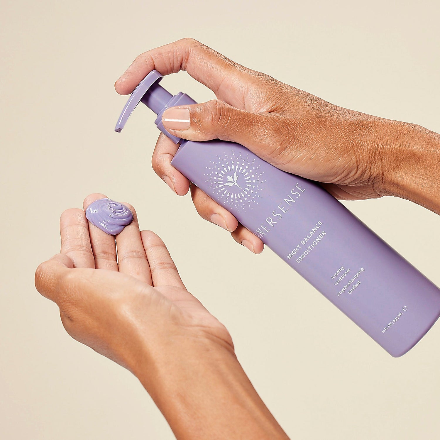 Hand holding a purple bottle of Innersense hair product with a beige background