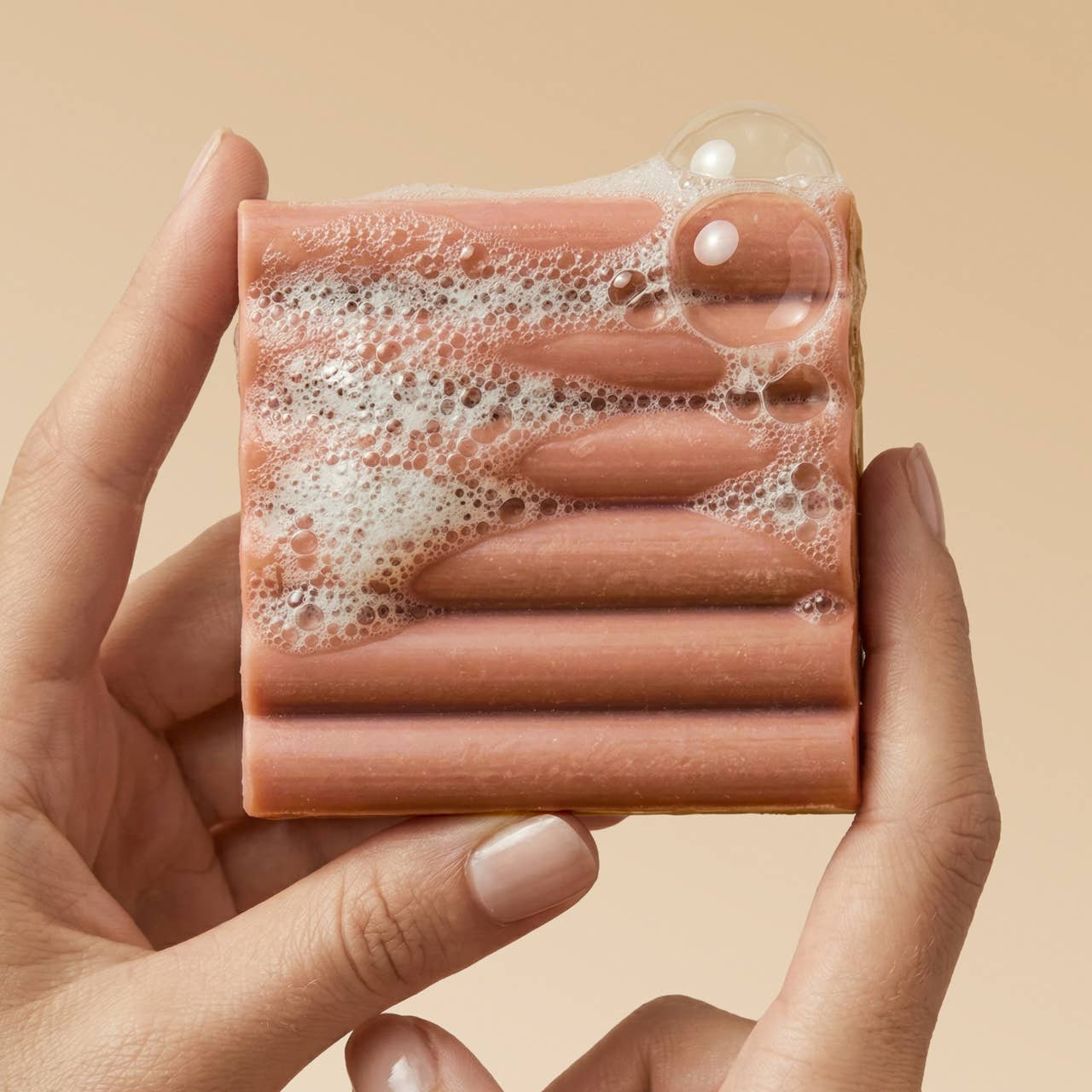 Hand holding a bar of Kitsch Amber Shores Body Wash Bar with bubbles against a beige background