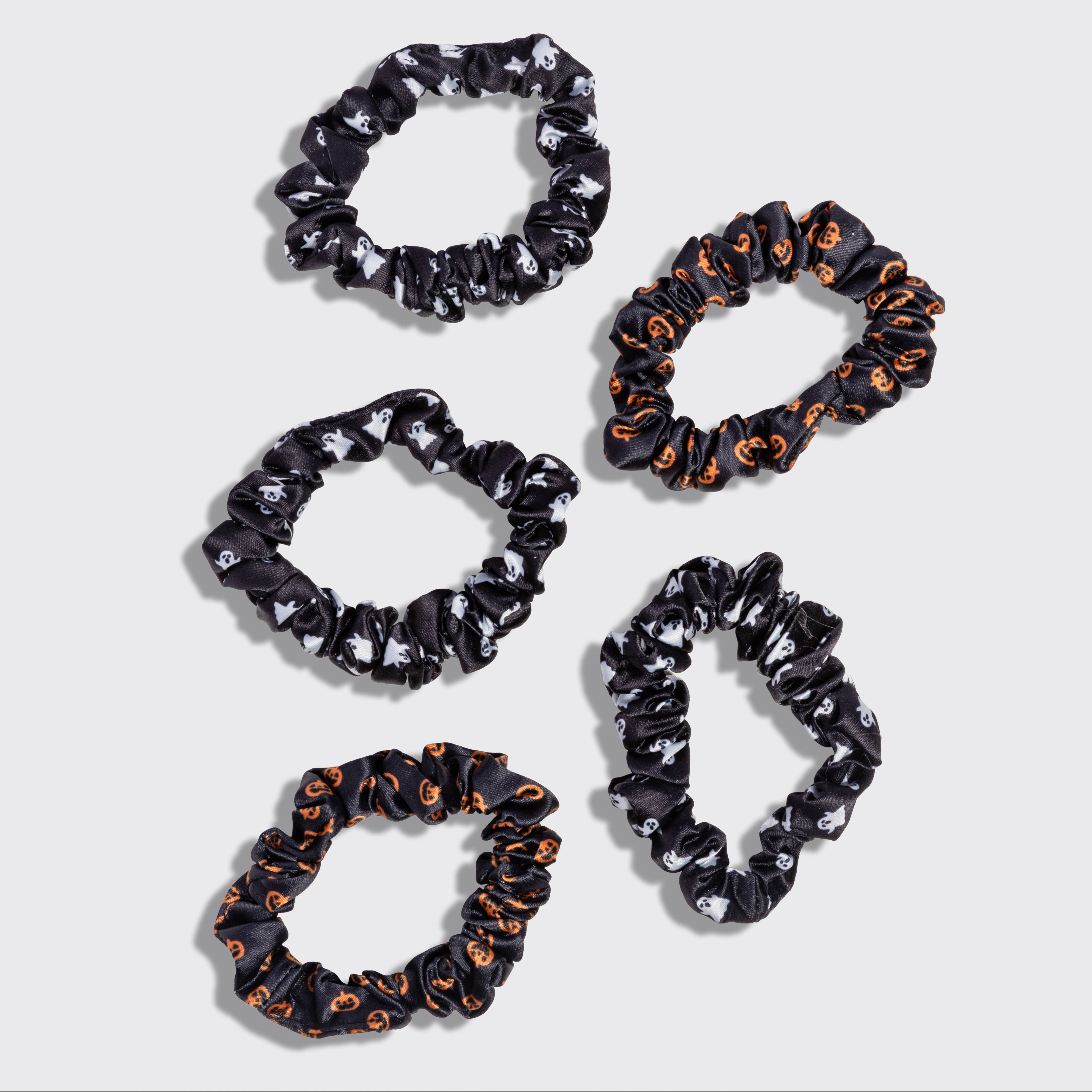 Five black fabric hair scrunchies with Halloween-themed patterns, including orange pumpkins and white skulls, arranged on a light gray background. Kitsch Ghost & Pumpkins Scrunchies