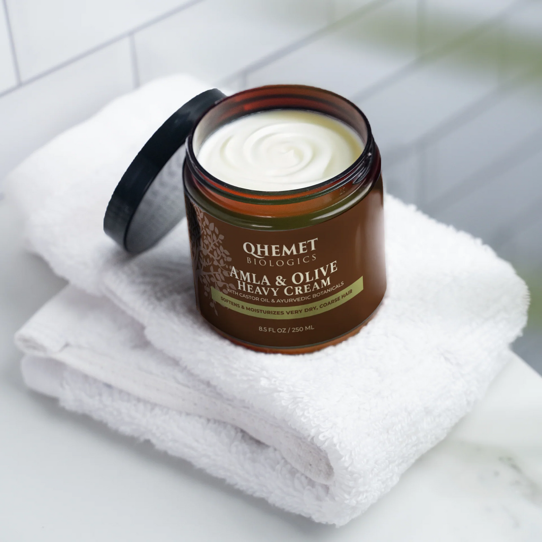 Jar of Qhemet Biologics Amla & Olive Heavy Cream on a white towel with a tiled wall background