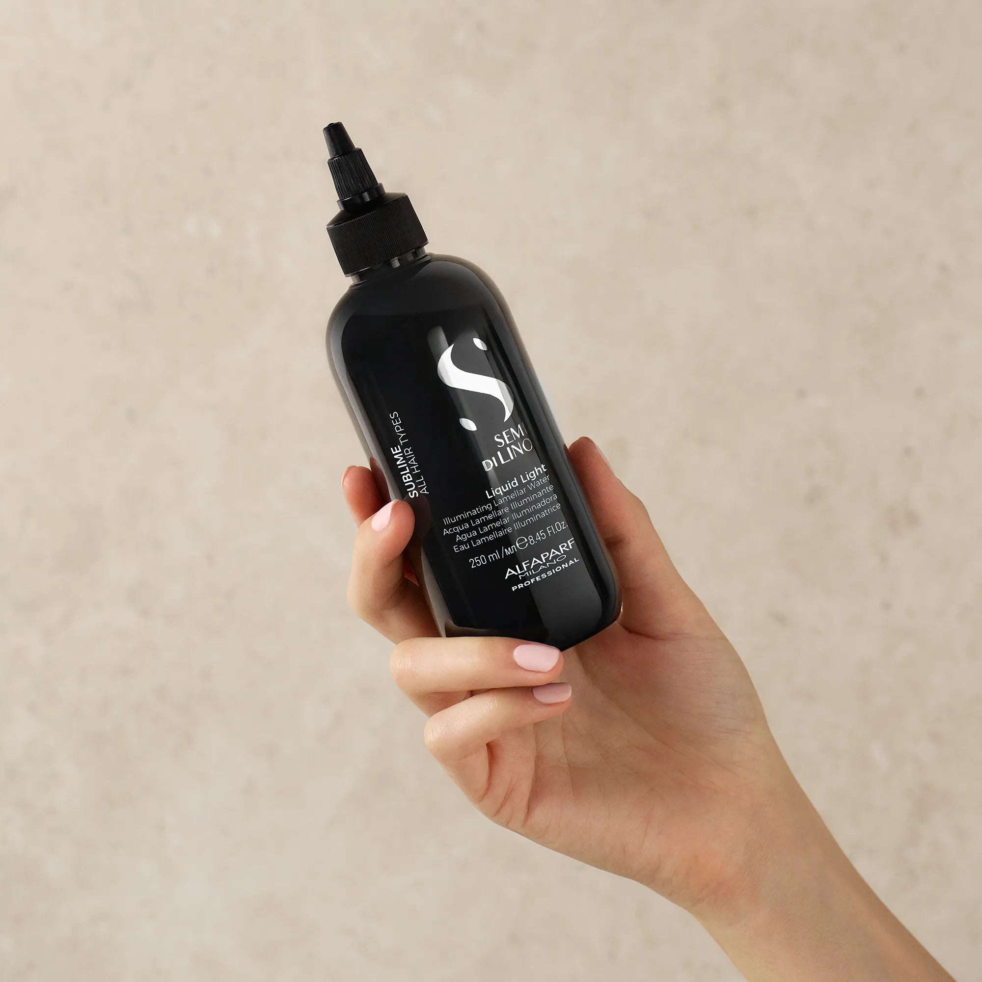 Close-up of Alfaparf Milano Semi di Lino Sublime Liquid Light Illuminating Lamellar Water 250ml in hand – lightweight lamellar hair treatment for instant shine, hydration and frizz control.
