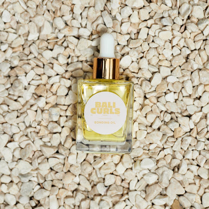 Small bottle OF BALI CURLS BONDING OIL with dropper on a textured beige surface