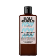 A bottle of Bali Curls ACV Clarifying Shampoo, featuring a dark amber-brown bottle and a black cap, set against a light blue arch background with white clouds.