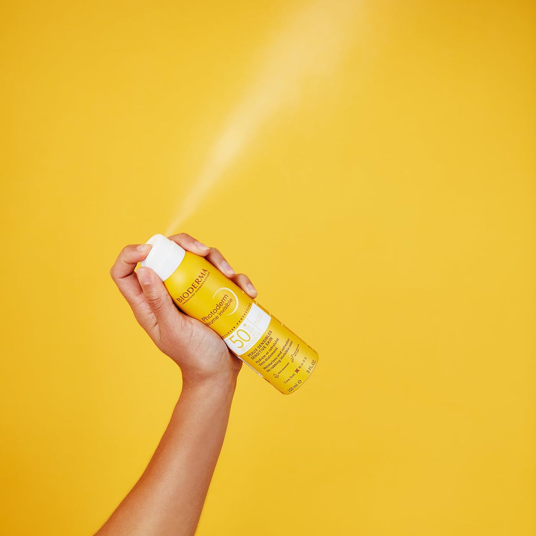 Bioderma Photoderm Invisible Mist SPF50+ 150ml hand spraying into air with yellow background