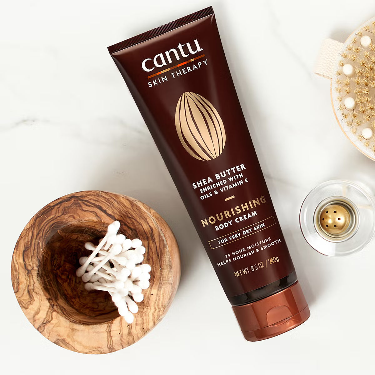 Cantu Skin Therapy Shea Butter Nourishing Body Cream 240g tube with shea butter body cream packaging displayed in a flat lay with skincare accessories