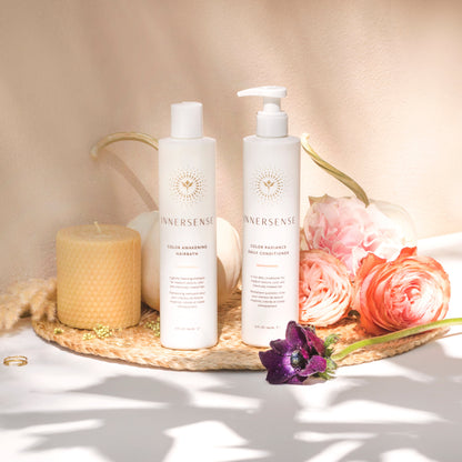 Two bottles of Innersense skincare products on a woven mat with flowers and a candle.