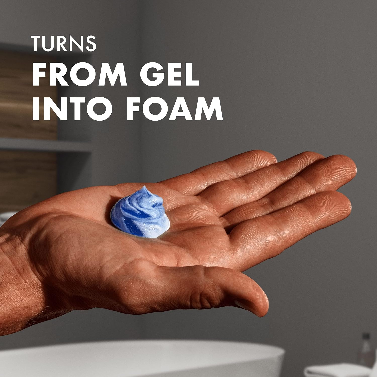 Blue Gillette Fusion shave gel transforming into rich white foam on a man’s palm against a softly lit grey bathroom background.