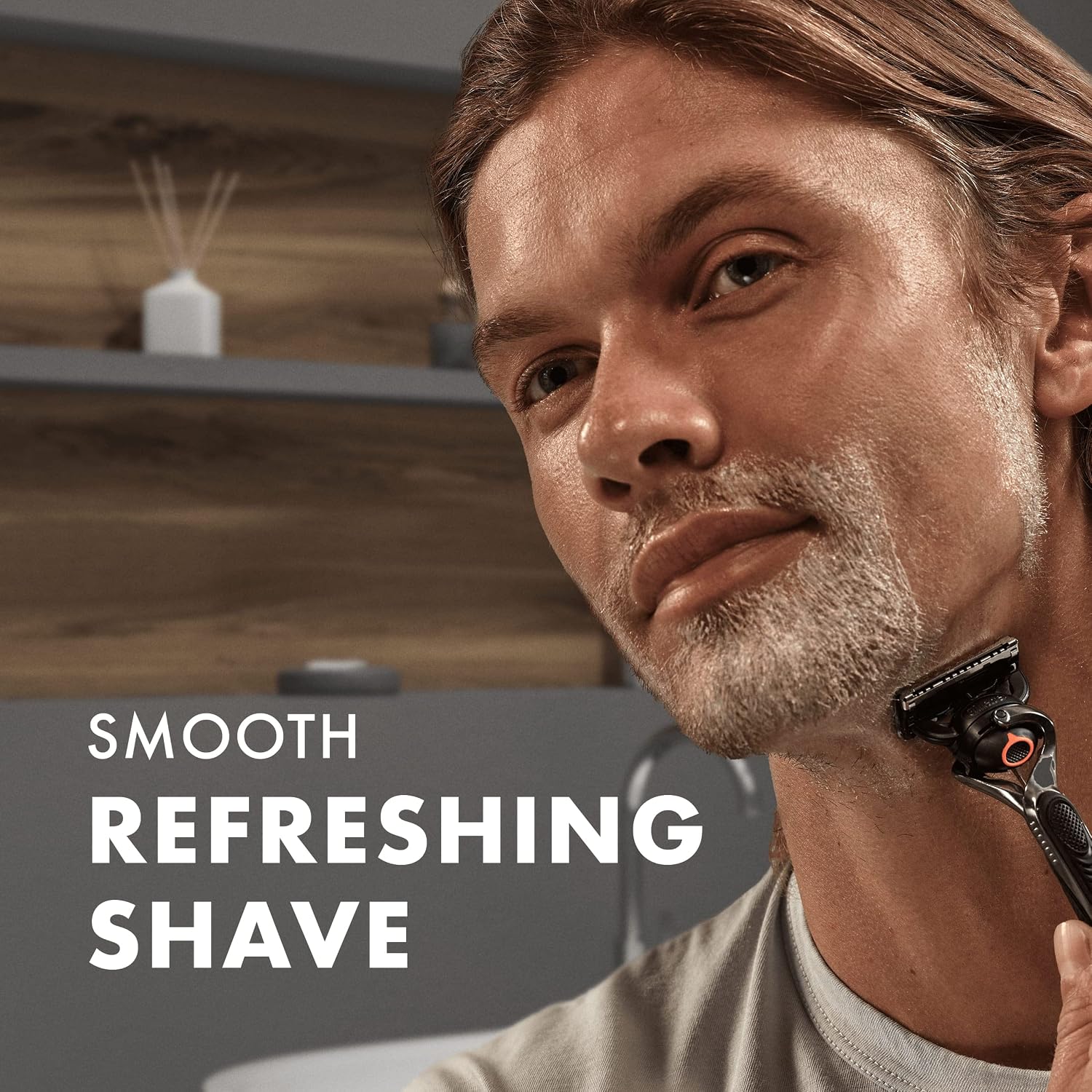 Man shaving foam-covered facial hair with a Gillette razor in a modern bathroom, illustrating a smooth, refreshing shave.