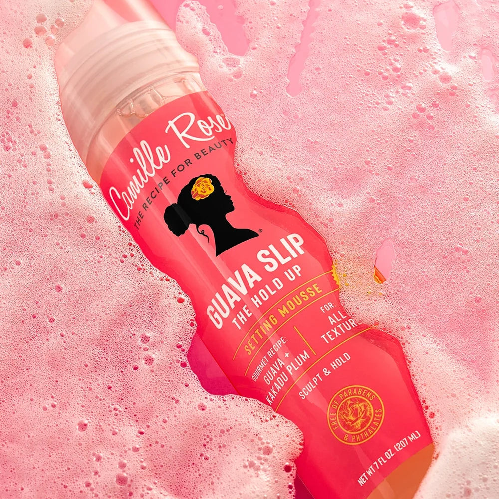 Pink bottle of Camille Rose Guava Slip Setting Mousse product on a pink foam background