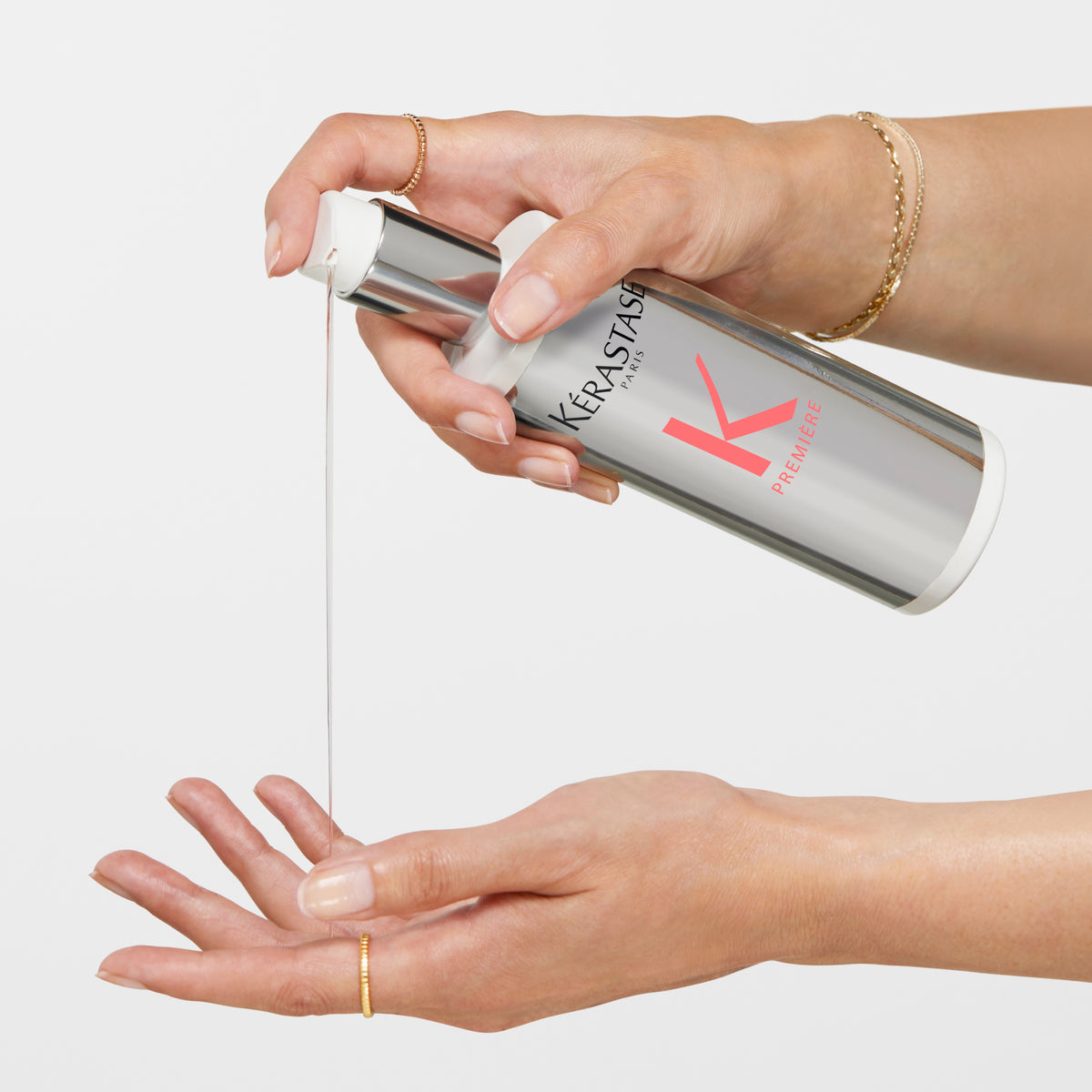 Person holding a Kérastase Première Concentré Décalcifiant Ultra-Réparateur Pre-Shampoo Treatment 250ml and dispensing it onto their hand against a white background