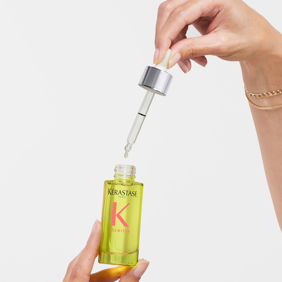 Kerastase serum bottle with dropper held by a hand on a light background