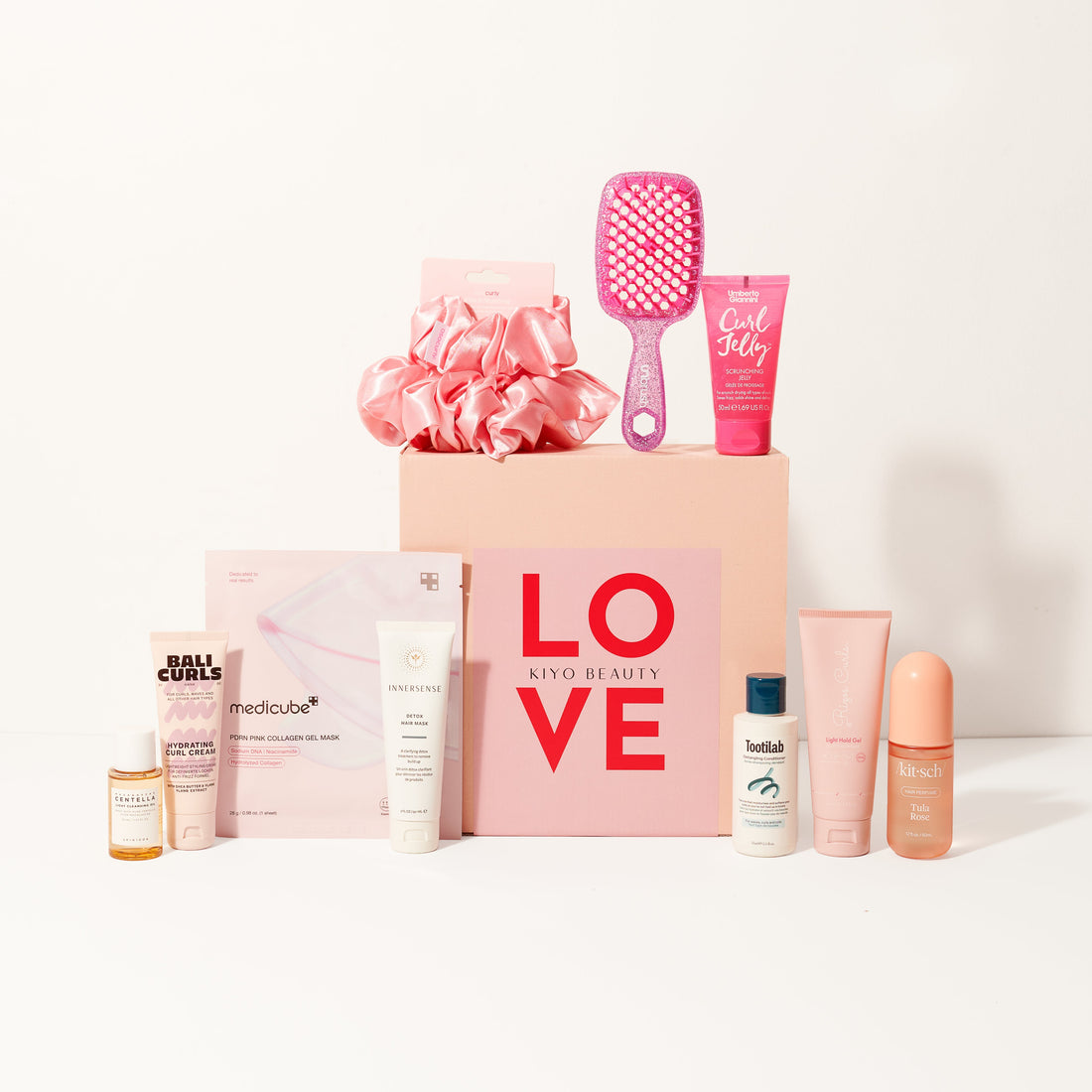 Collection of beauty products including bottles, a brush, and a pink box with &