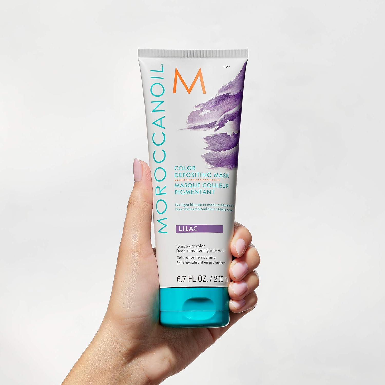 white hand holding Moroccanoil Color Depositing Mask Lilac 200ml