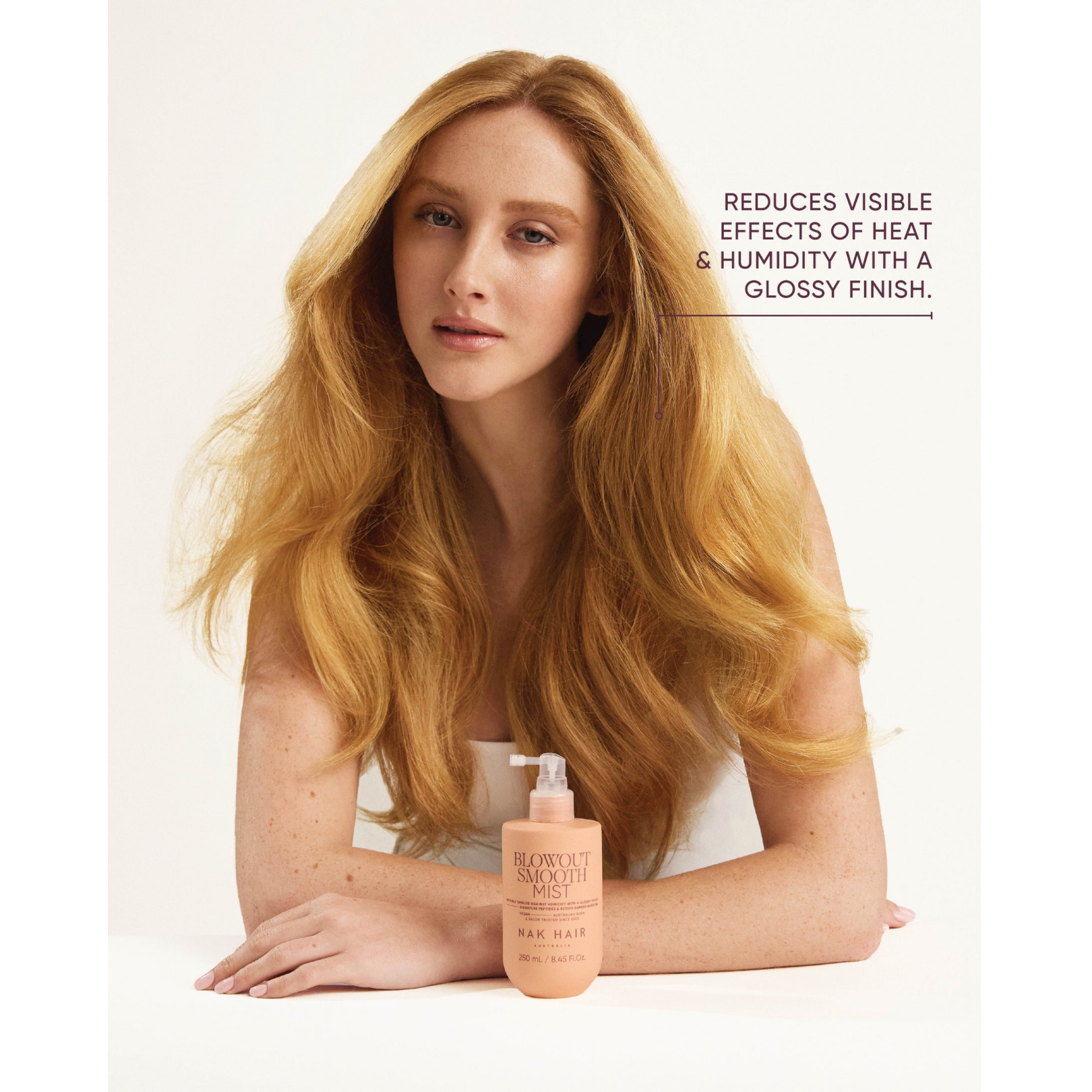 Woman with a smooth, glossy blonde blowout beside NAK Hair Blowout Smooth Mist 250ml, formulated to reduce the visible effects of heat and humidity