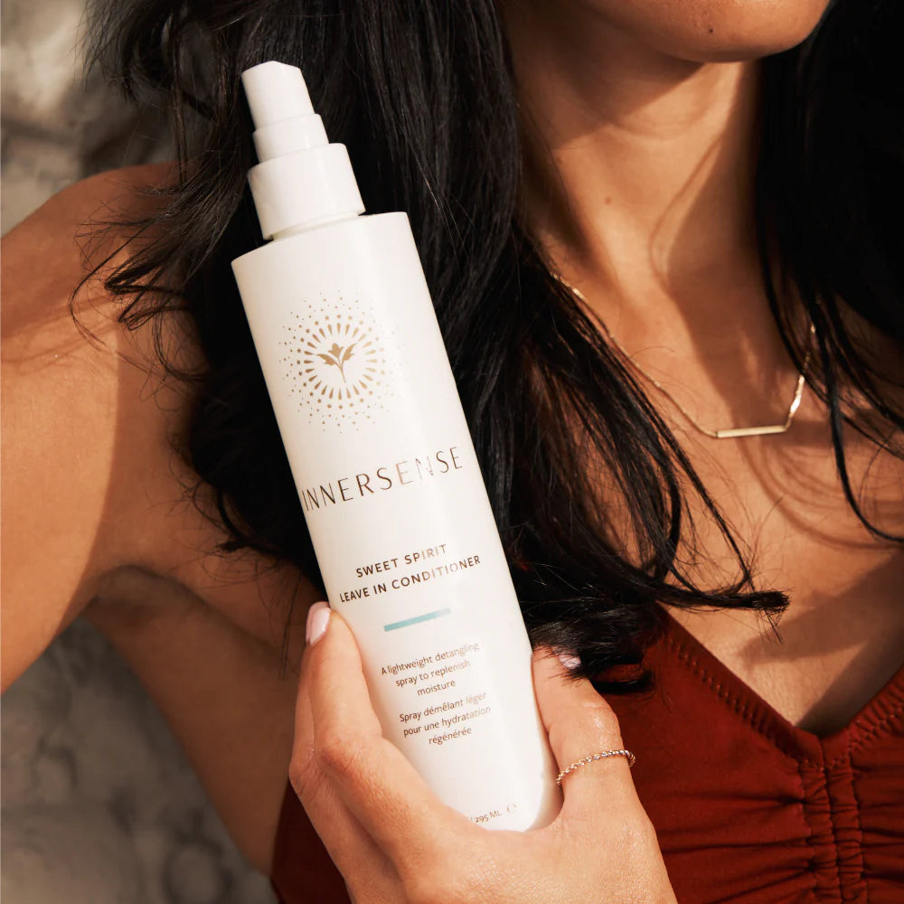 Person holding a bottle of Inner Sense Sweet Spirit Leave-In Conditioner with blurred background