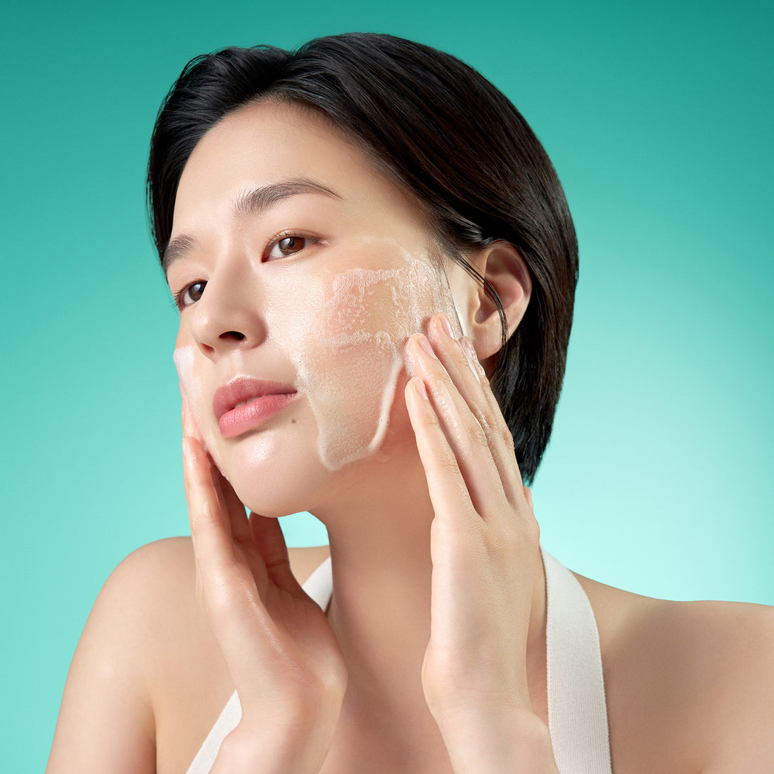 Woman applying a face mask against a teal background