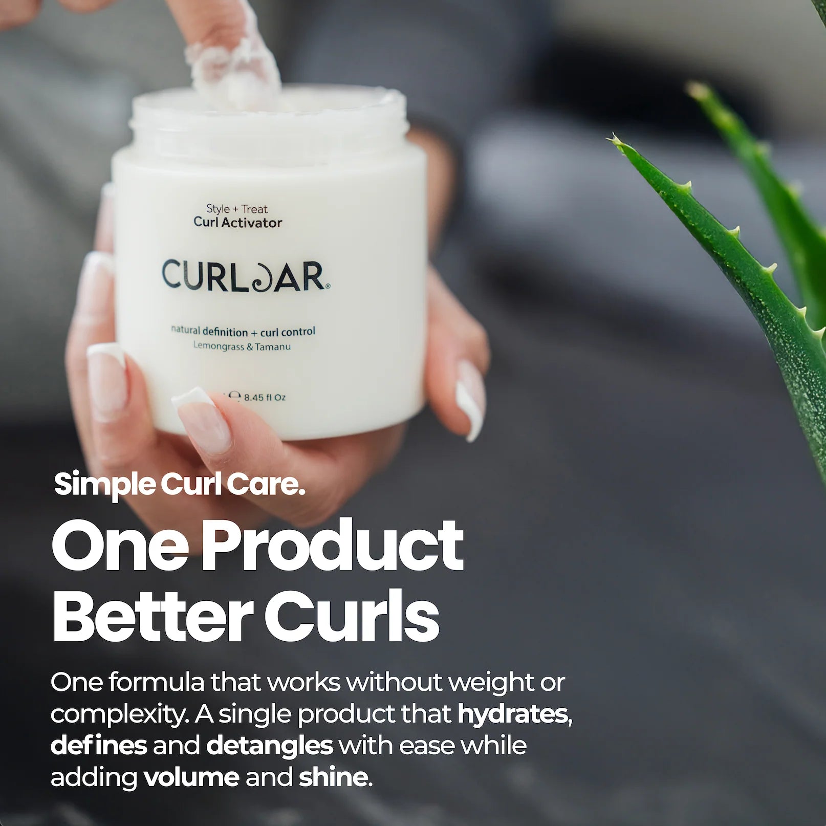 A hand holding a white jar of CURLBAR Curl Activator with a clear top, shown with promotional text on a dark gray background and a green aloe plant in the corner.