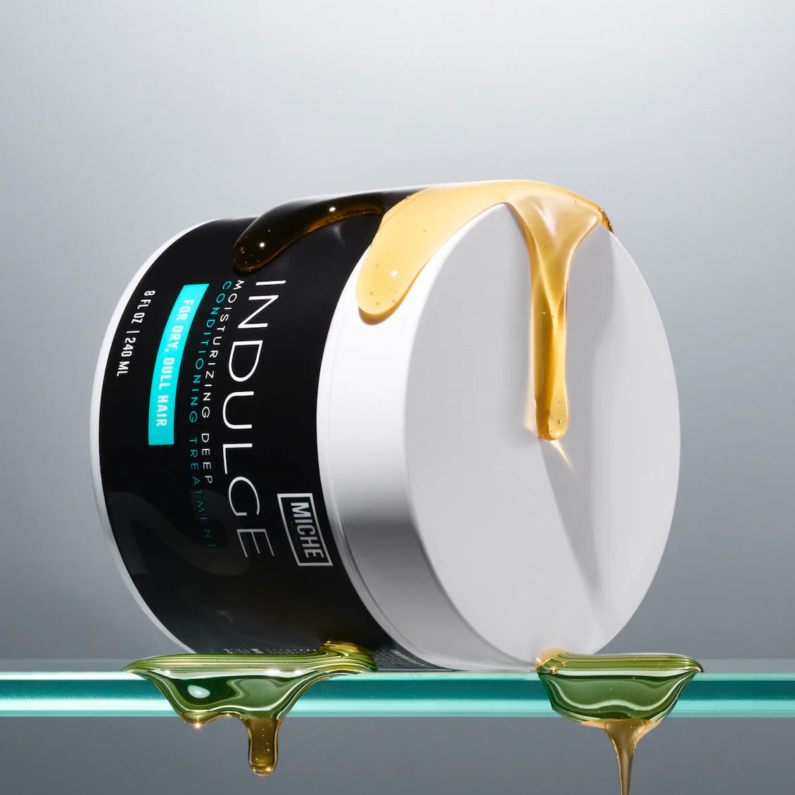 Jar of Indulge skincare product with gold cream oozing out on a gray background