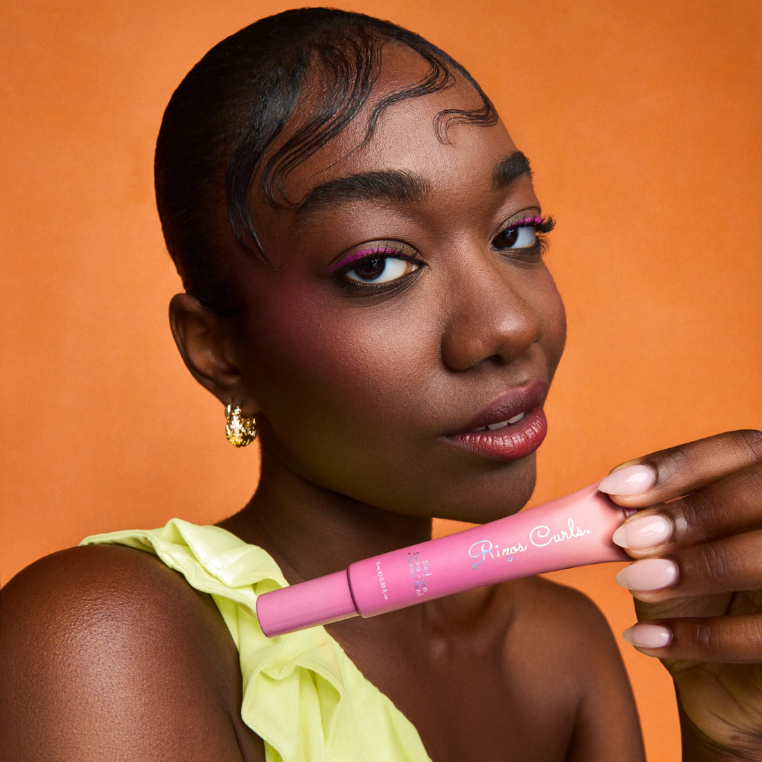 Rizos Curls Sleek Styling Cream an Taming Wand with Woman holding a pink hair product against an orange background